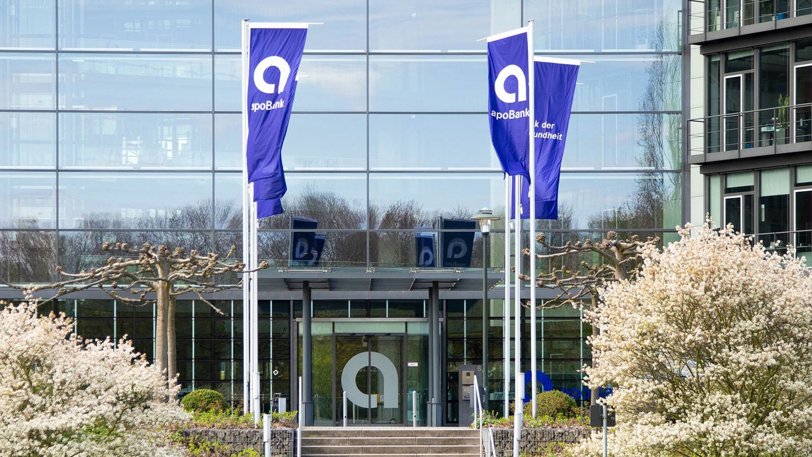 apoBank – Zentrale in Düsseldorf mit blauen Fahnen vor der Glasfassade (Unternehmensfoto)